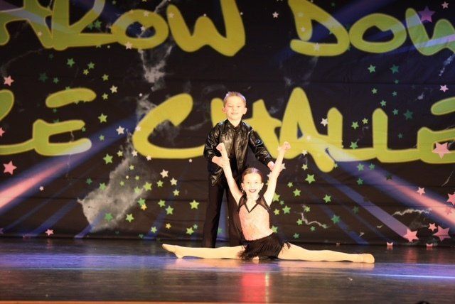 Two dancers in black and pink pose on a stage with a colorful starry backdrop