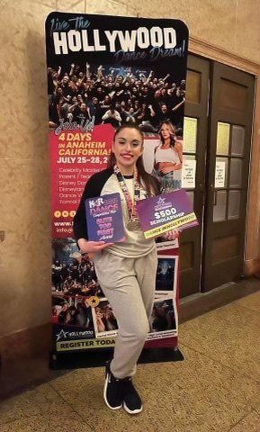 Woman posing in front of a Hollywood poster, holding two colorful books and smiling indoors