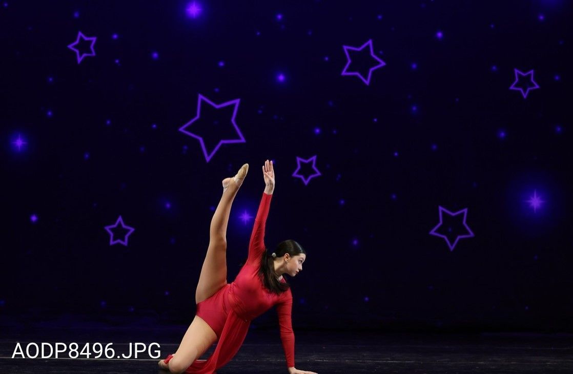 Dancer in red costume striking a floor pose against a dark stage with purple star graphics