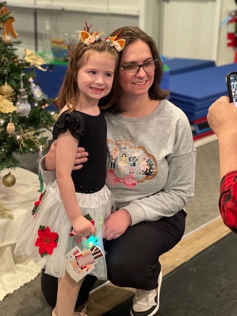Woman kneeling with smiling child at a holiday event beside a decorated Christmas tree