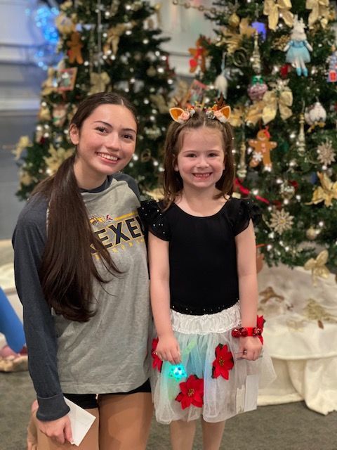 Two smiling children posing in front of a decorated Christmas tree.