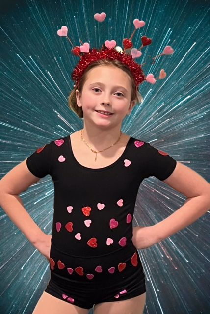 Girl wearing black shirt decorated with pink hearts, hands on hips, against a blue starburst background