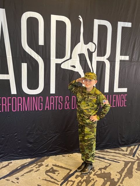 Child in camouflage costume standing onstage at ASPIRE Performing Arts & Dance Challenge.