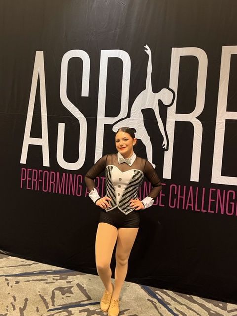 Young dancer in a black costume posing in front of an ASPPIRE performance challenge backdrop.