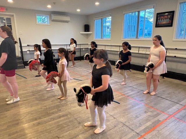 Children in a dance class practice poses in a studio with mirrors and wooden floors.