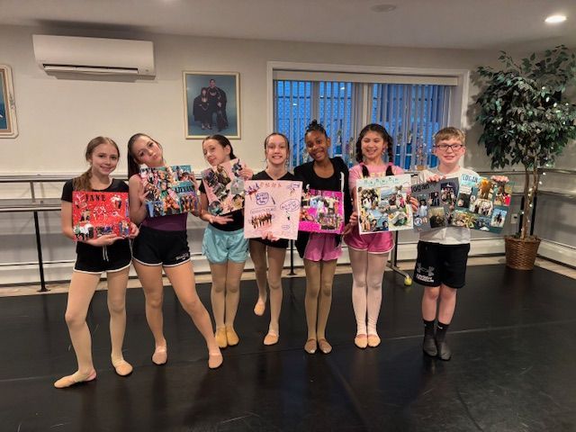 Group of dancers holding decorated posters in a studio, standing in a line and smiling.