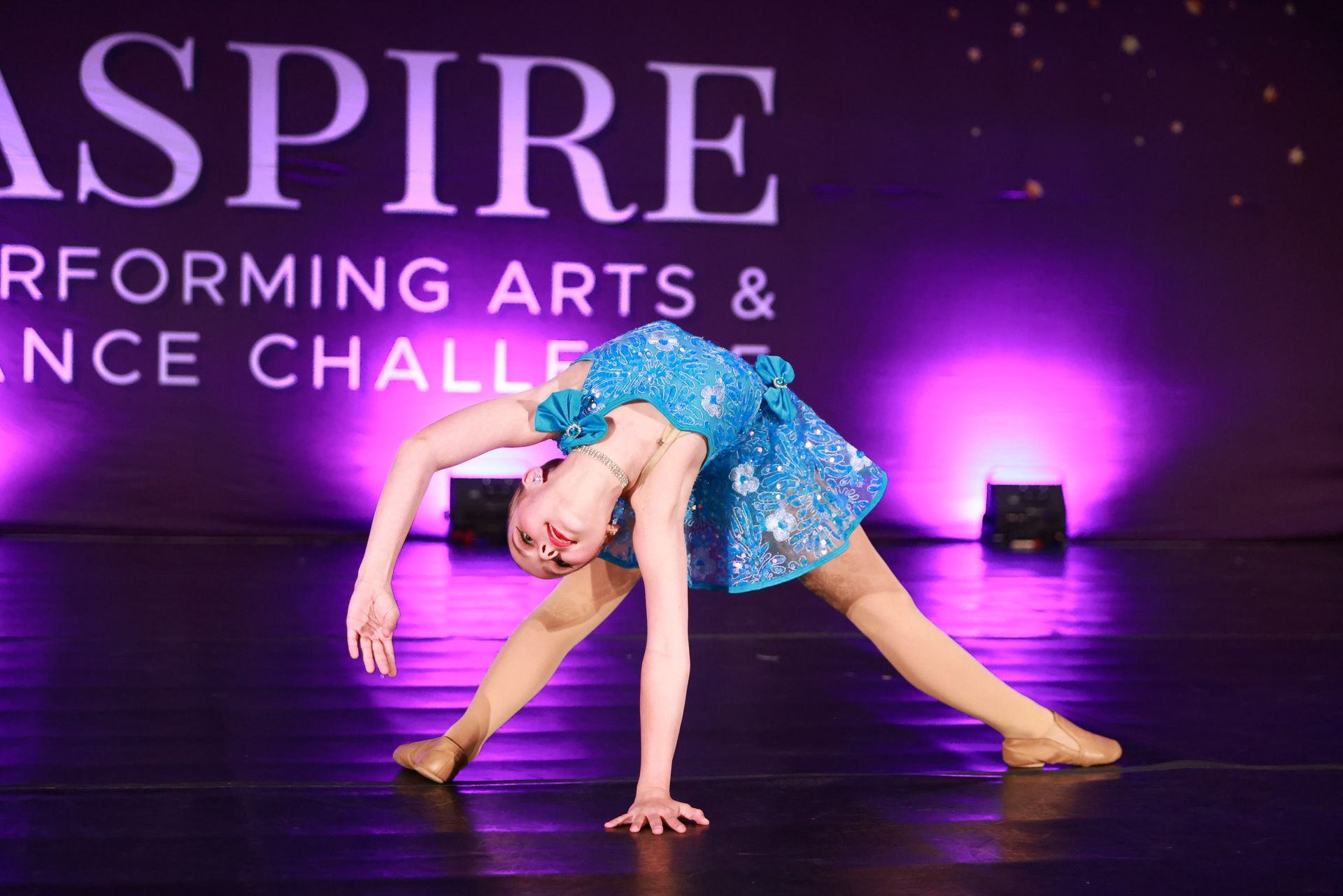 Young dancer in a blue costume striking a floor pose on a lit stage during a dance competition