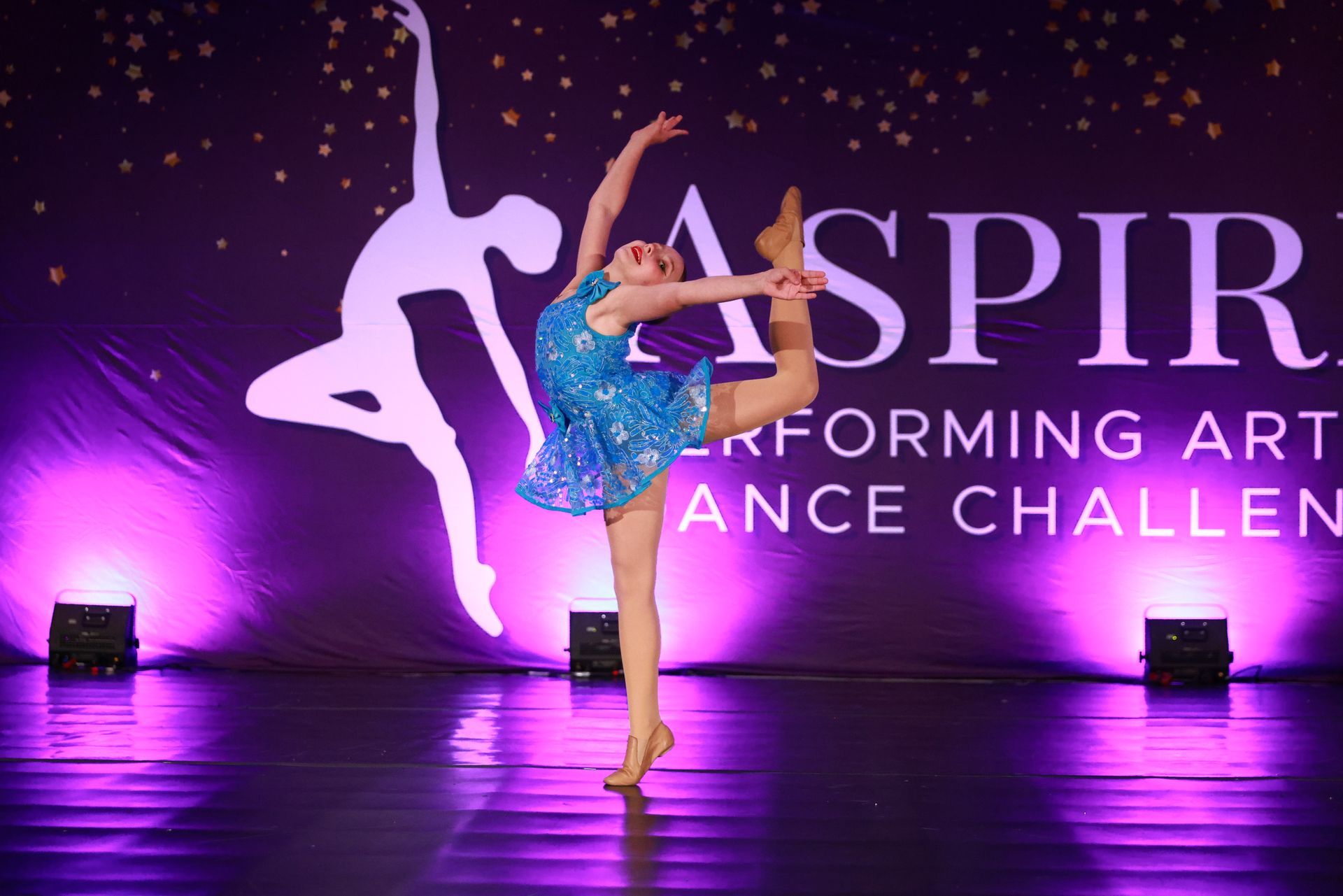 Contemporary dancer in blue costume striking a high leg pose on a purple-lit stage with ASPIR text backdrop