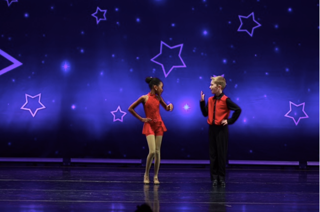 Two performers on stage in red costumes against a purple starry backdrop