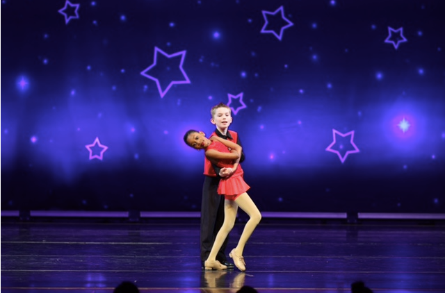 Two dancers in red and black costumes posing on a stage with glowing purple star lights