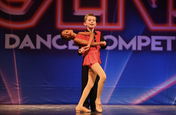 Two dancers in pink costumes posing on a stage at a dance competition