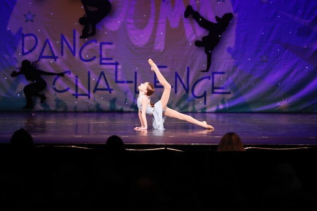 Two dancers in white pose onstage under purple lights at Dance Challenge competition