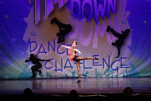 Solo dancer center stage in pink costume, with silhouetted dancers and “Dance Challenge” backdrop