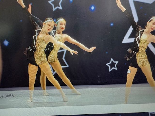 Two young dancers in gold costumes performing onstage against a starry black backdrop
