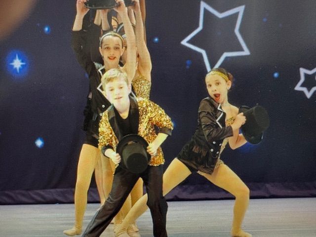 Three dancers in black and gold costumes posing mid-performance on a stage with star-shaped lights.