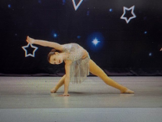 Contortionist in a gray leotard balancing on one hand on a stage with starry backdrop
