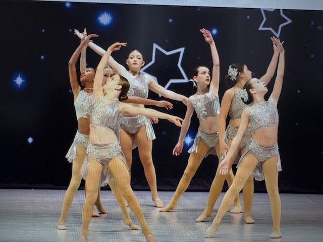 Group of dancers in silver costumes performing a synchronized routine on a stage with star decorations