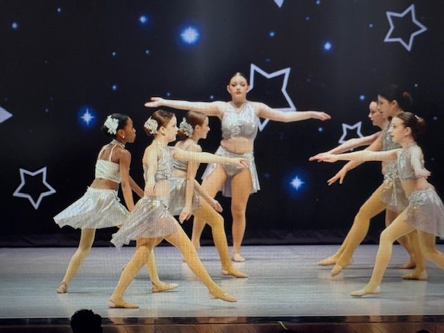 Dance troupe performing on stage in silver costumes against a starry black backdrop