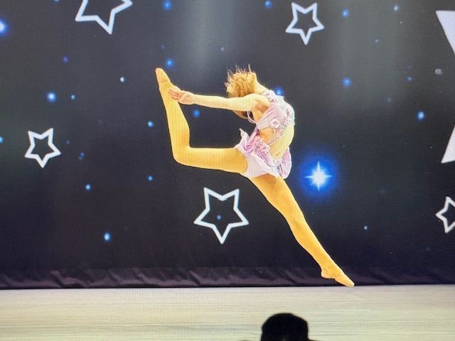 Young gymnast in a pink leotard performs a high leap on stage with starry backdrop