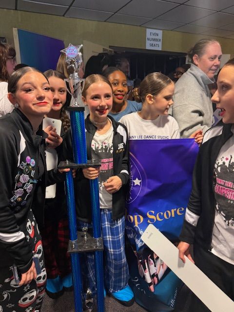 Group of smiling students holding a blue trophy and purple banner at an indoor event