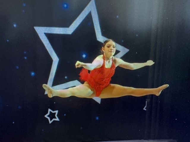 Dancer in a red dress performing a split leap against a starry black backdrop