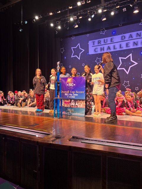 Children onstage holding a banner at a dance challenge event with starry backdrop and audience behind them