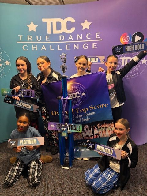 Young dancers holding awards and a trophy at the True Dance Challenge stage backdrop