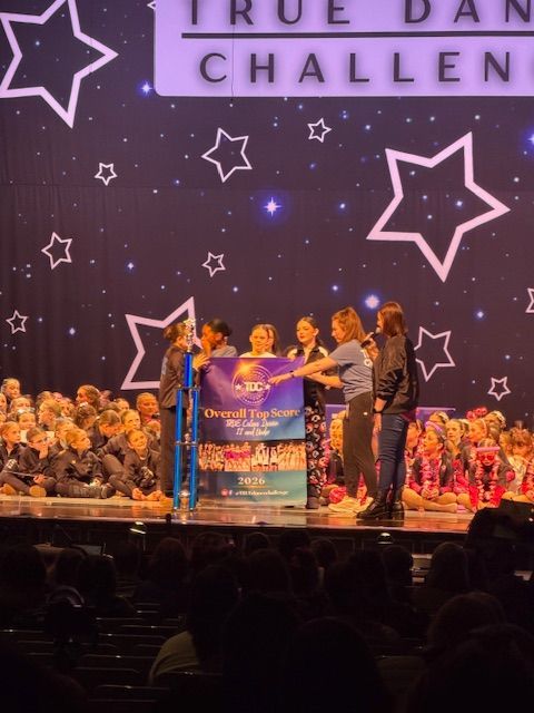Dance competition award ceremony onstage with people holding a banner under star decorations and bright lights