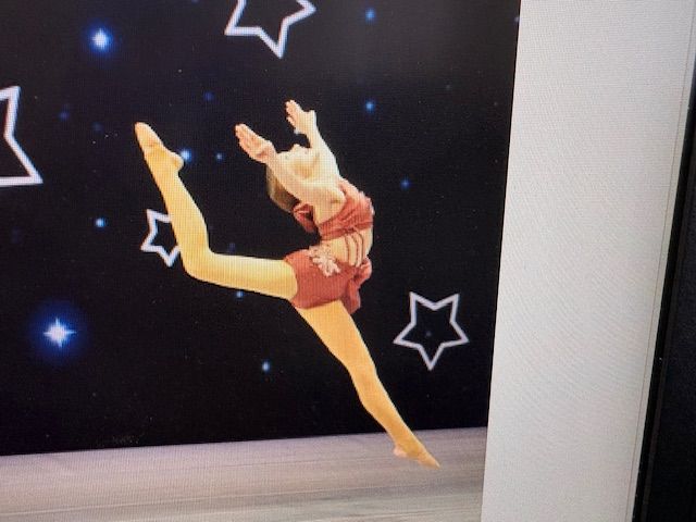 Young dancer in a red costume performs a high leap on a stage with starry black backdrop.