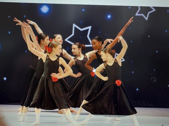 Young ballet dancers in black dresses performing onstage with star-shaped lights in the background