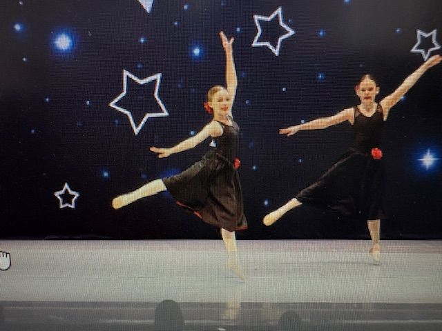 Two ballet dancers onstage in black outfits, posing against a starry backdrop.