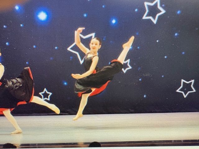 Ballet dancers on stage in black and red costumes against a starry backdrop, one leg lifted high