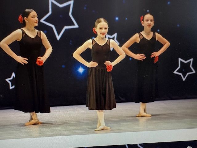 Three dancers in black dresses with red gloves pose on stage before a starry backdrop.