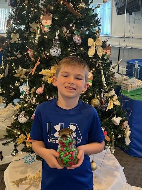 Child holding a jar of candy in front of a decorated Christmas tree