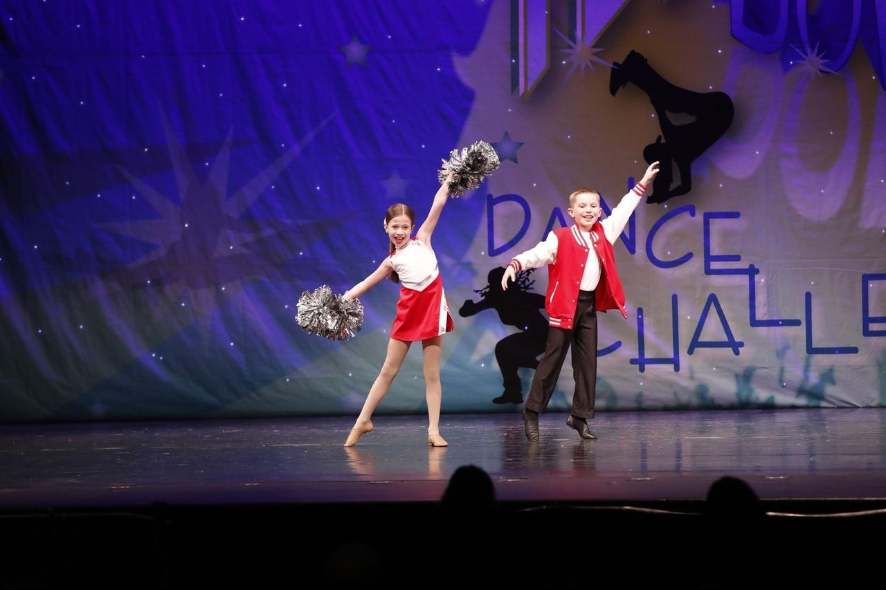 Two dancers in red and white costumes performing on a lit stage with a purple backdrop