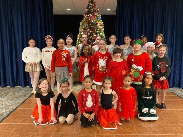 Children in festive costumes posing in rows in front of a decorated Christmas tree.
