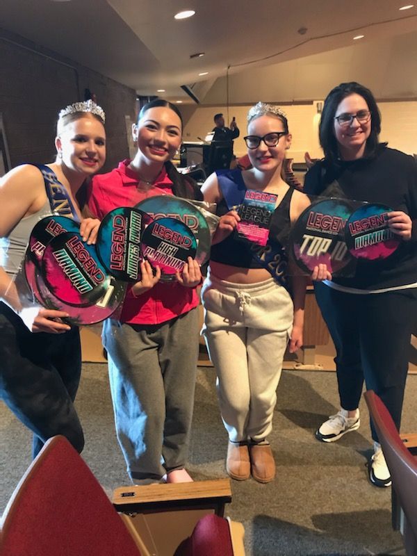 Four people standing indoors, smiling and holding colorful patterned signs in a conference room.