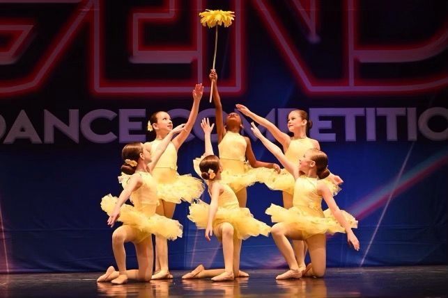Young dancers in yellow costumes striking a cheer pose on a competition stage
