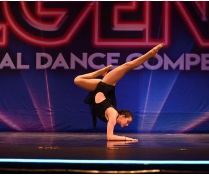 Contortionist balancing on one forearm in a black outfit on a stage with purple lighting