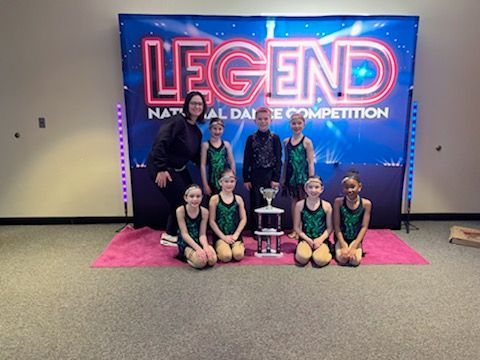 Group of dancers posing with a trophy in front of a “LEGEND” competition banner