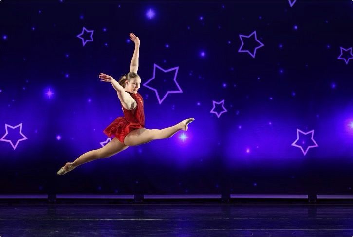 Dancer leaping in a red costume on a purple starry stage background