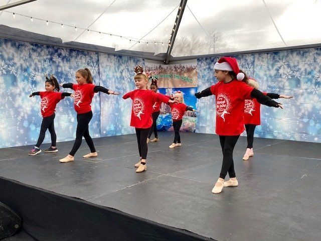 Children in red shirts perform a dance on an outdoor stage with a winter backdrop.