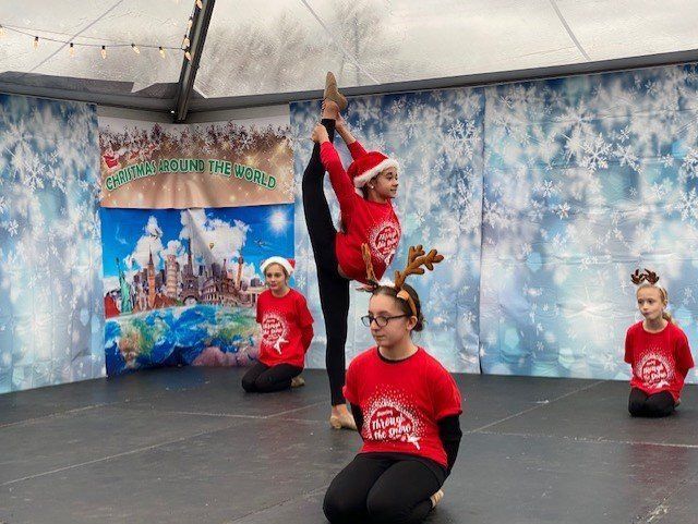 Children in red shirts pose and dance on an outdoor stage with a blue winter mural backdrop.