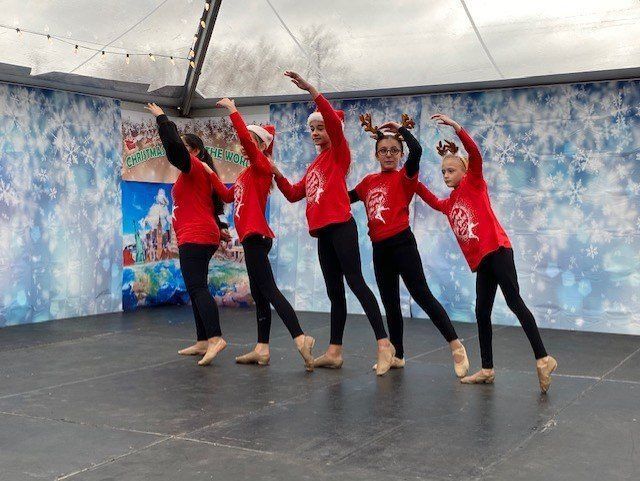 Five dancers in red shirts pose on a stage with arms raised against a blue backdrop.