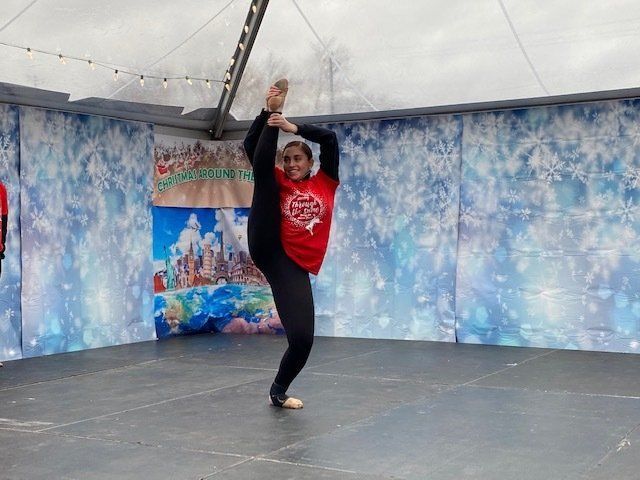 Dancer in red and black costume performing a high leg hold on an outdoor stage