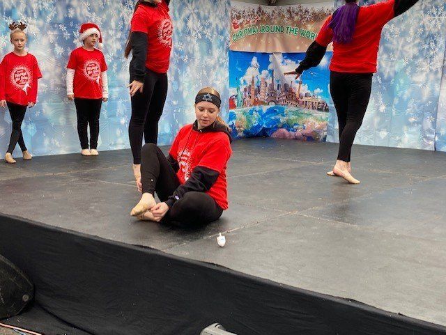 Children in red shirts perform a dance on a stage with a winter backdrop