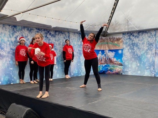 Five dancers in red shirts performing on a stage under a white tent