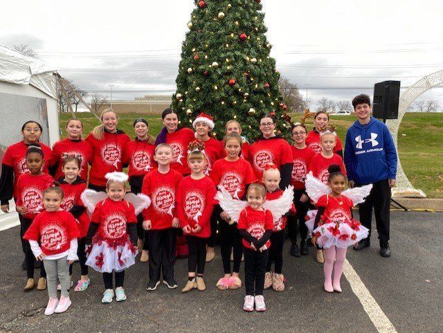 Group of children in red shirts posing in front of a decorated Christmas tree outdoors