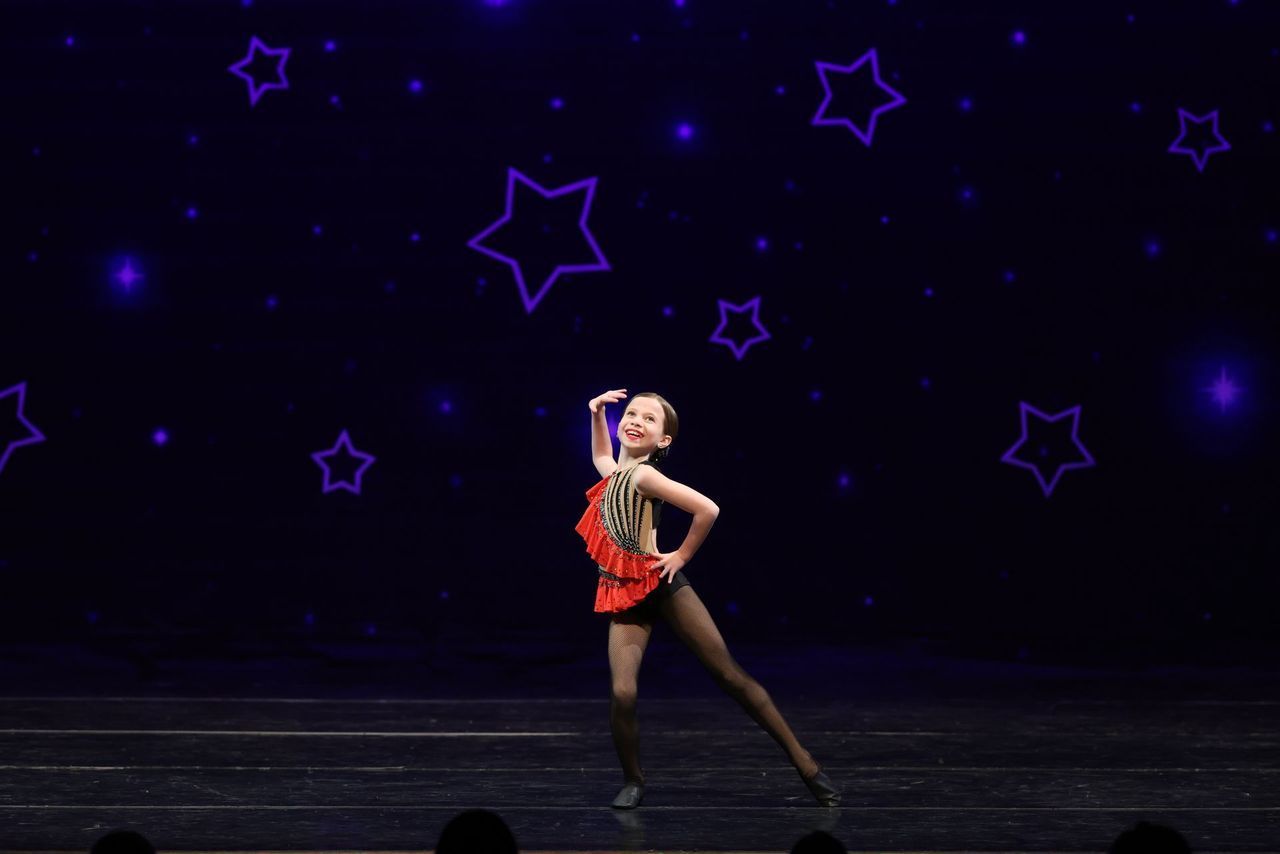 Solo dancer in red and black costume posing on a stage with purple starry lights