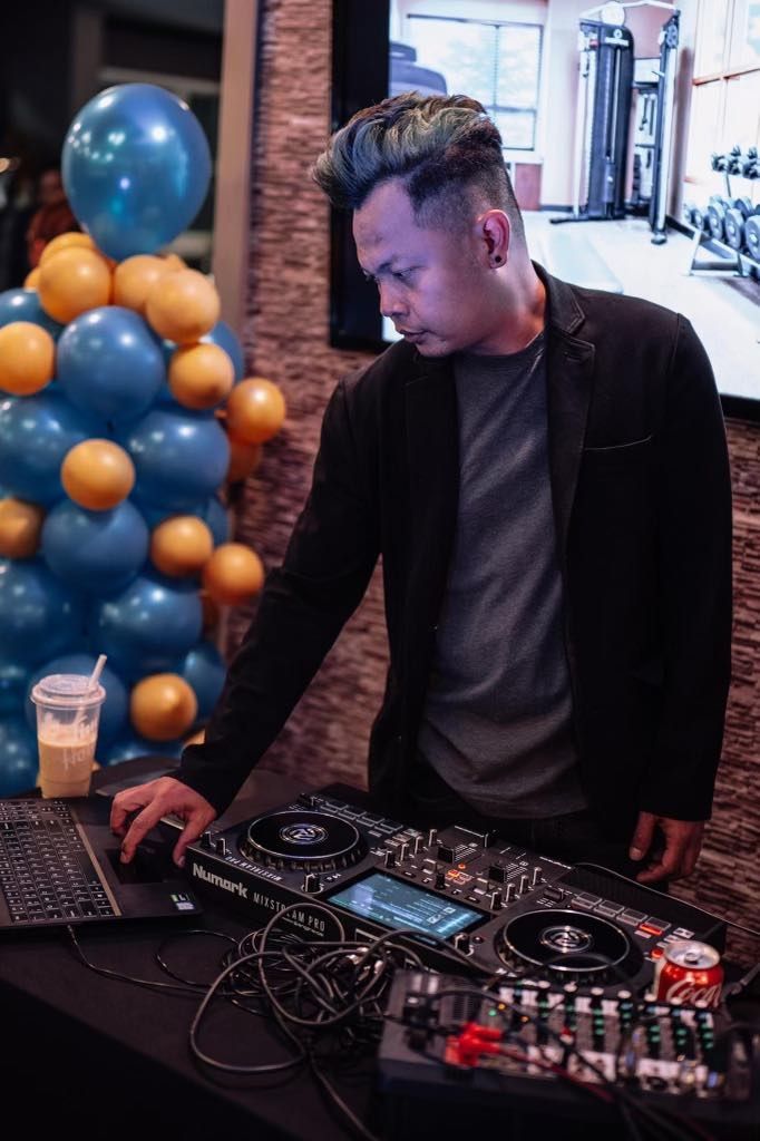 Man operating DJ equipment beside blue and orange balloon decorations at an indoor event